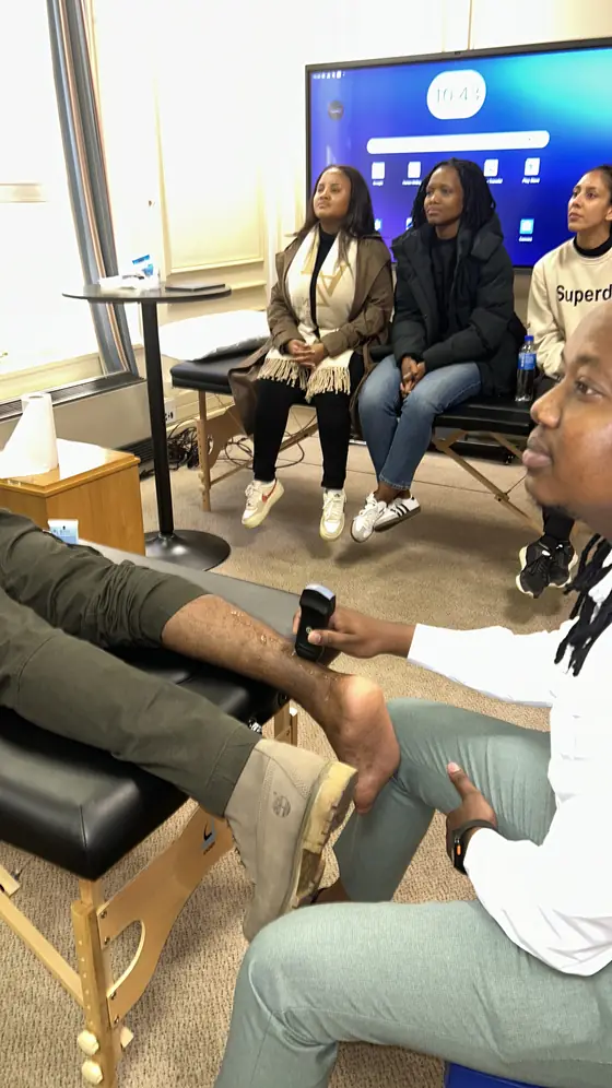 Learner performing an ankle scan with a handheld probe while colleagues observe