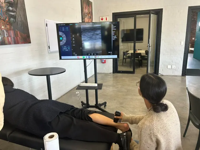 Learner scanning a lower limb with a handheld Doppler-enabled ultrasound device, image displayed on screen